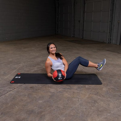 Woman doing sit ups with exercise ball on workout mat medicine ball red and black body solid