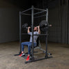 man doing shoulder presses on black squat rack